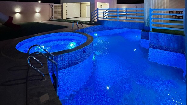 A swimming pool with a blue-lit edge, a metal ladder, and a modern building in the background.