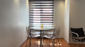 A dining area with a round table, clear chairs, and a window with blinds. - Curated Living in Nişantaşı (Istanbul)