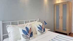 A bedroom with a white bed, two decorative pillows, a blue lamp, and a wooden wardrobe. - Curated Living in Nişantaşı (Istanbul)