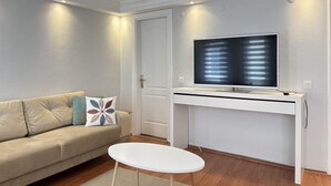 A living room with a sofa, a small round table, a TV on a white stand, and a door. - Curated Living in Nişantaşı (Istanbul)