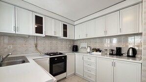 A kitchen with white cabinets, a gas stove, a coffee maker, and a kettle. - Curated Living in Nişantaşı (Istanbul)