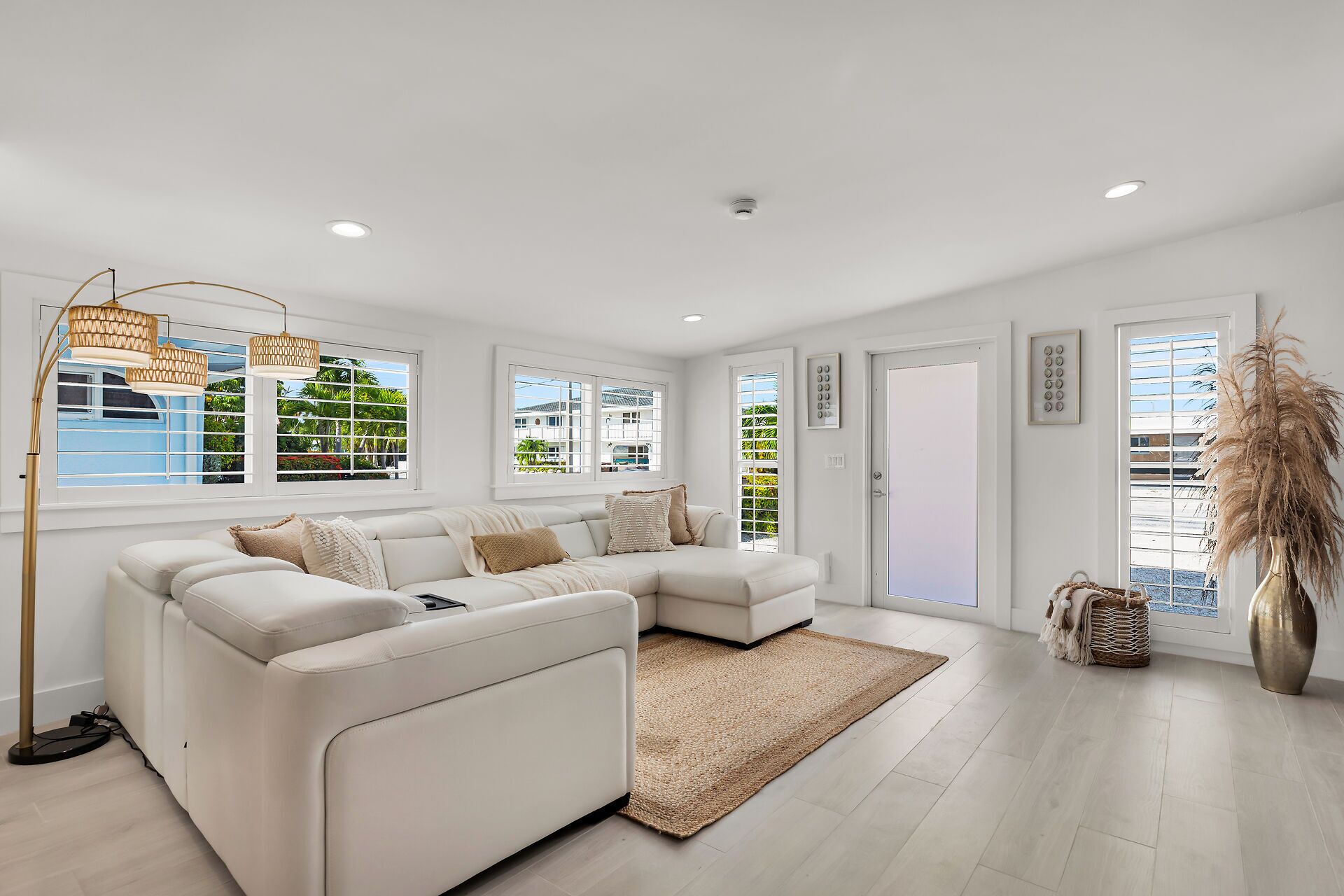 A modern living room with a white sectional sofa, large windows, a floor lamp, and a decorative vase.