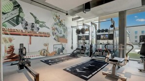 Et fitnessrum med træningsudstyr, et muralmaleri og store vinduer.