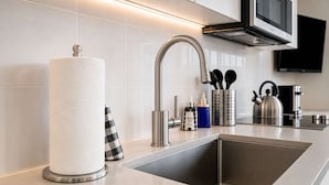 Et moderne køkken med en stålvask, papirhåndklædeholder, sæbedispenser og elkedel.