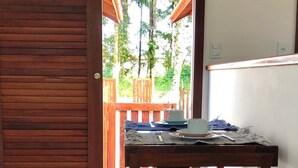 A wooden table with a bench, a door, and a view of greenery outside.