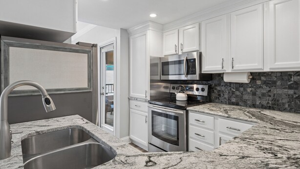 A modern kitchen with white cabinets, stainless steel appliances, and a granite countertop. - Near Beach Coastal Getaway (Hilton Head Island)