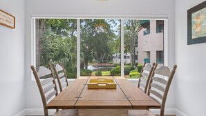 A dining area with a wooden table, chairs, and a view of greenery and buildings outside. - Near Beach Coastal Getaway (Hilton Head Island)