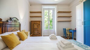 Un dormitorio con cama, cabecero de madera, armario, escritorio y ventana con vistas a la vegetación.