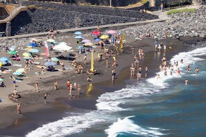 Une plage où l’on peut voir des gens se prélasser au soleil et se baigner, des parasols et une côte rocheuse.