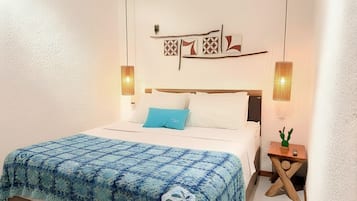 A neatly made bed with a blue blanket, two wall-mounted lamps, and a small wooden nightstand with a cactus.