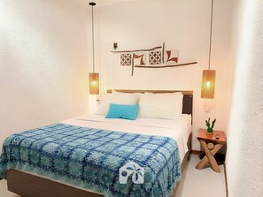 A neatly made bed with a blue blanket, two wall-mounted lamps, and a small wooden nightstand with a cactus.