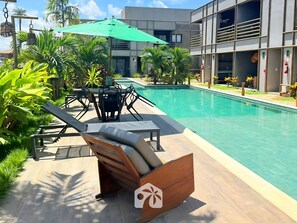 A swimming pool area with lounge chairs, a table, and an umbrella.