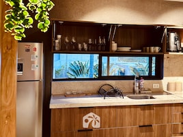 Cozinha moderna com janela integrada, eletrodomésticos de aço inoxidável e armários de madeira.