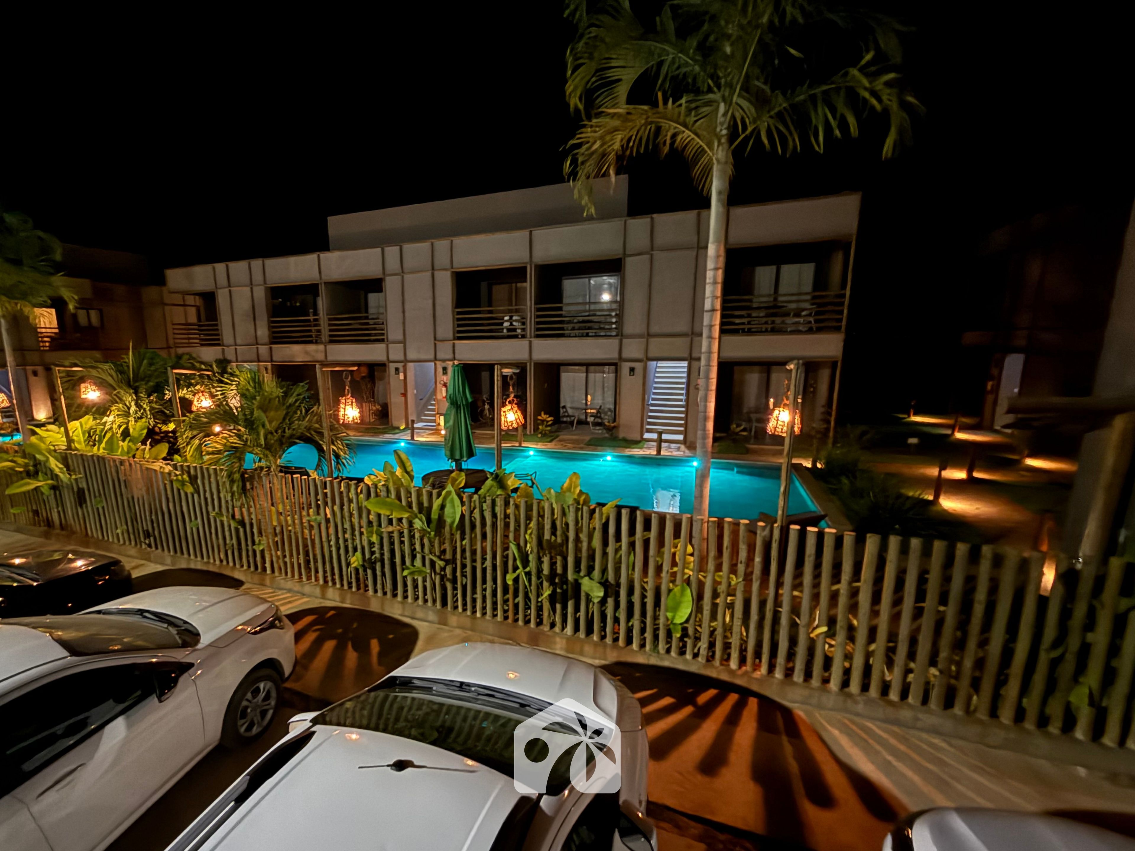 A hotel with a swimming pool, multiple balconies, and a parking area with cars.