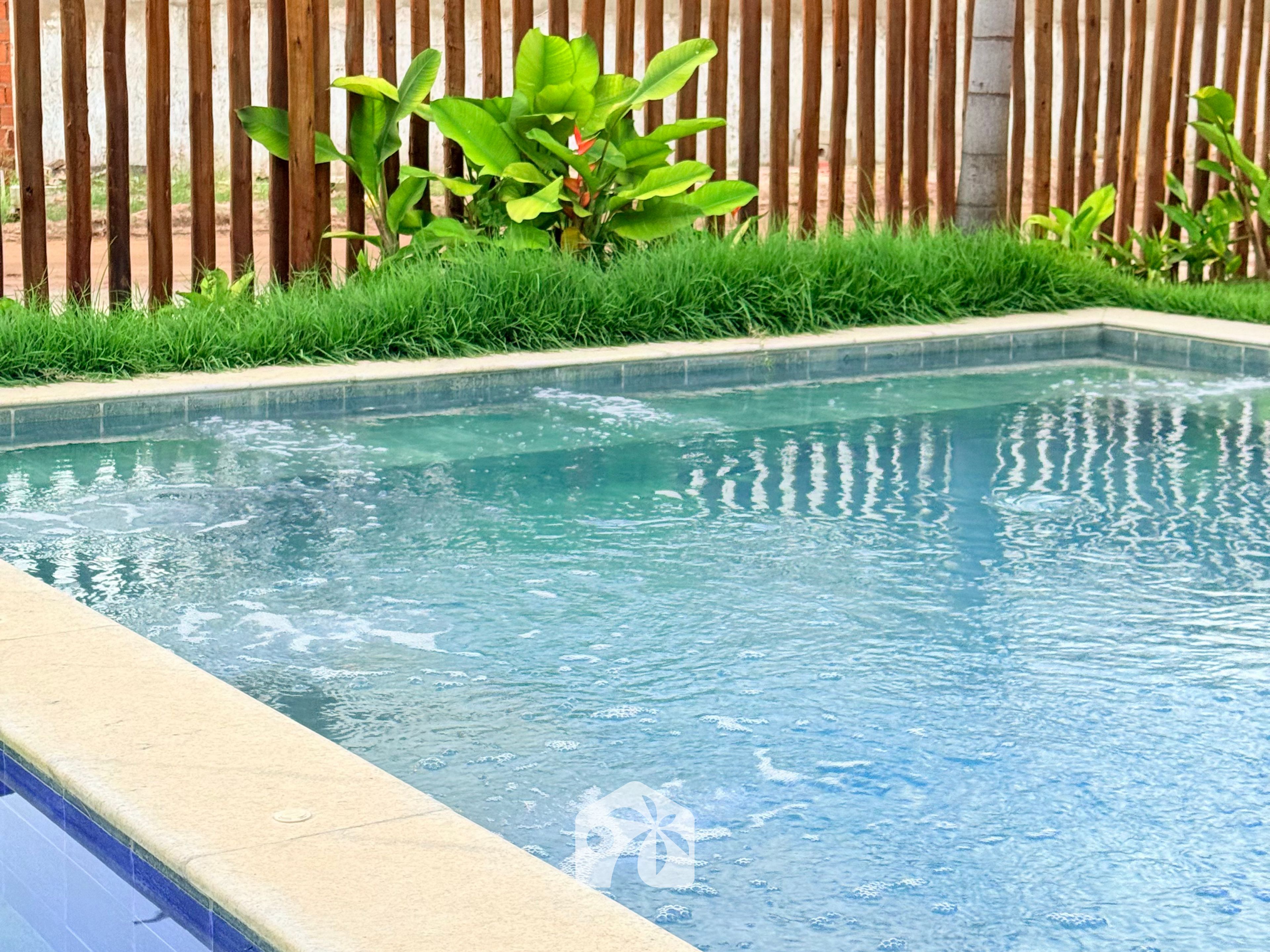 A rectangular swimming pool with clear water, surrounded by a concrete edge and a wooden fence in the background.