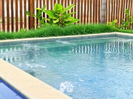 Una piscina rectangular con agua cristalina, rodeada por un borde de hormigón y una valla de madera al fondo.