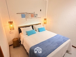 Una cama bien hecha con colcha azul y blanca, dos almohadas y un cabecero de madera.