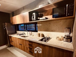 A modern kitchen with wooden cabinets, a built-in microwave, a coffee maker, a gas stove, and a blender.