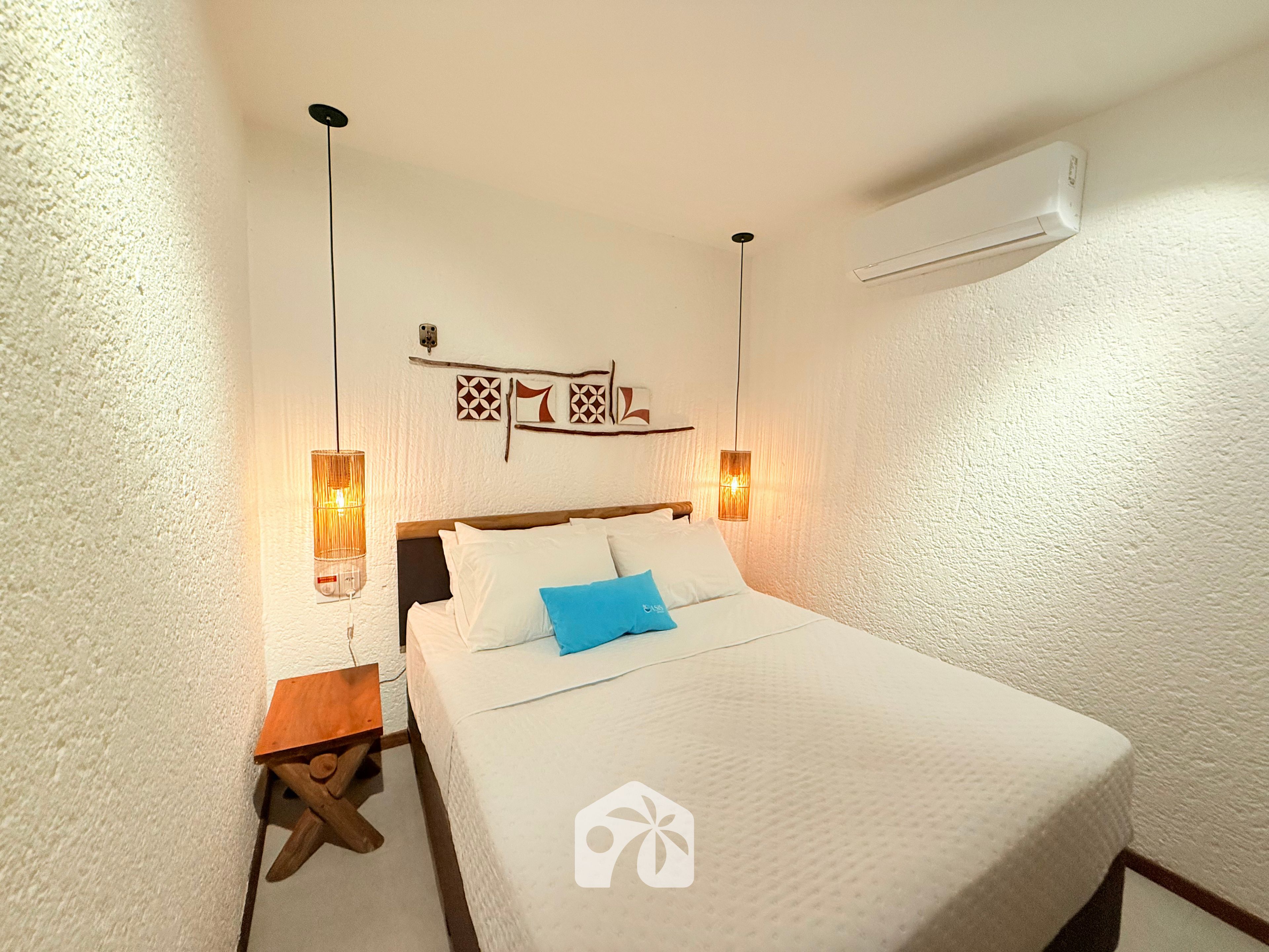 Quarto de hotel com cama, mesas de cabeceira, luminárias fixadas na parede e um objeto decorativo na parede.