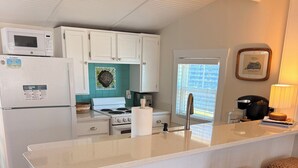 Una cocina con una isla central, armarios blancos, microondas y tostadora. Hay tres taburetes trenzados en la isla.