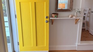 Una puerta amarilla brillante, un pequeño estante con adornos y un piso de madera.