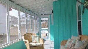 Un porche cubierto con muebles de mimbre, una decoración con forma de estrella de mar y vistas a casas a través de grandes ventanales.