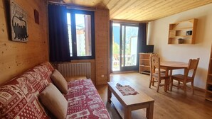 A wooden interior with a sofa, a table, and chairs, a TV on a stand, and a bookshelf. - Cabin studio with mountain view (Les Deux Alpes)