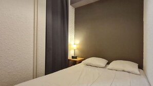 A hotel room with a bed, a nightstand, a lamp, and a dark curtain. - Cabin studio with mountain view (Les Deux Alpes)