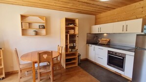 A compact kitchen with wooden cabinets, a built-in oven, and a dining area with a round table and chairs. - Cabin studio with mountain view (Les Deux Alpes)