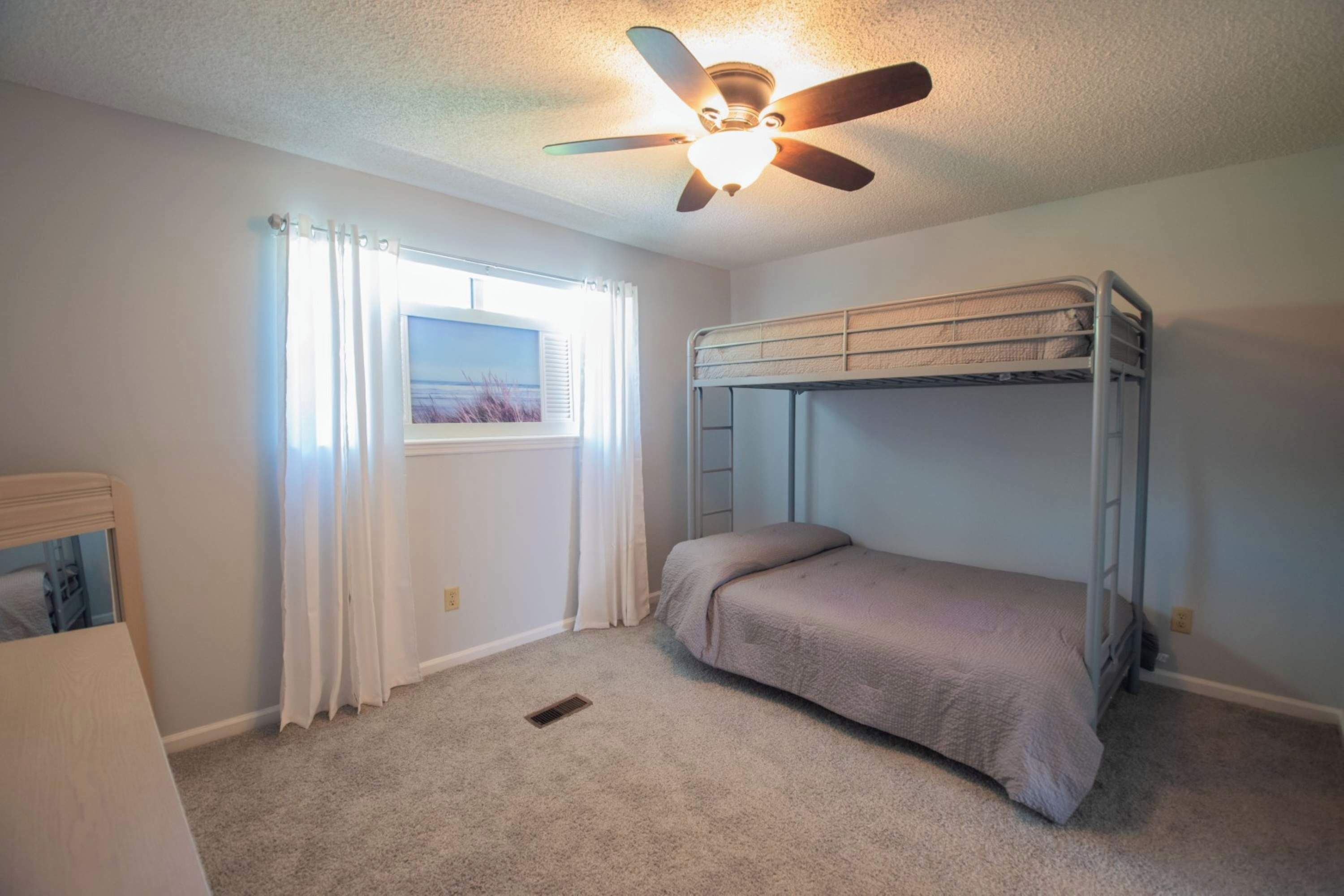 A bedroom with a bunk bed, a ceiling fan, a window with curtains, and a carpeted floor.