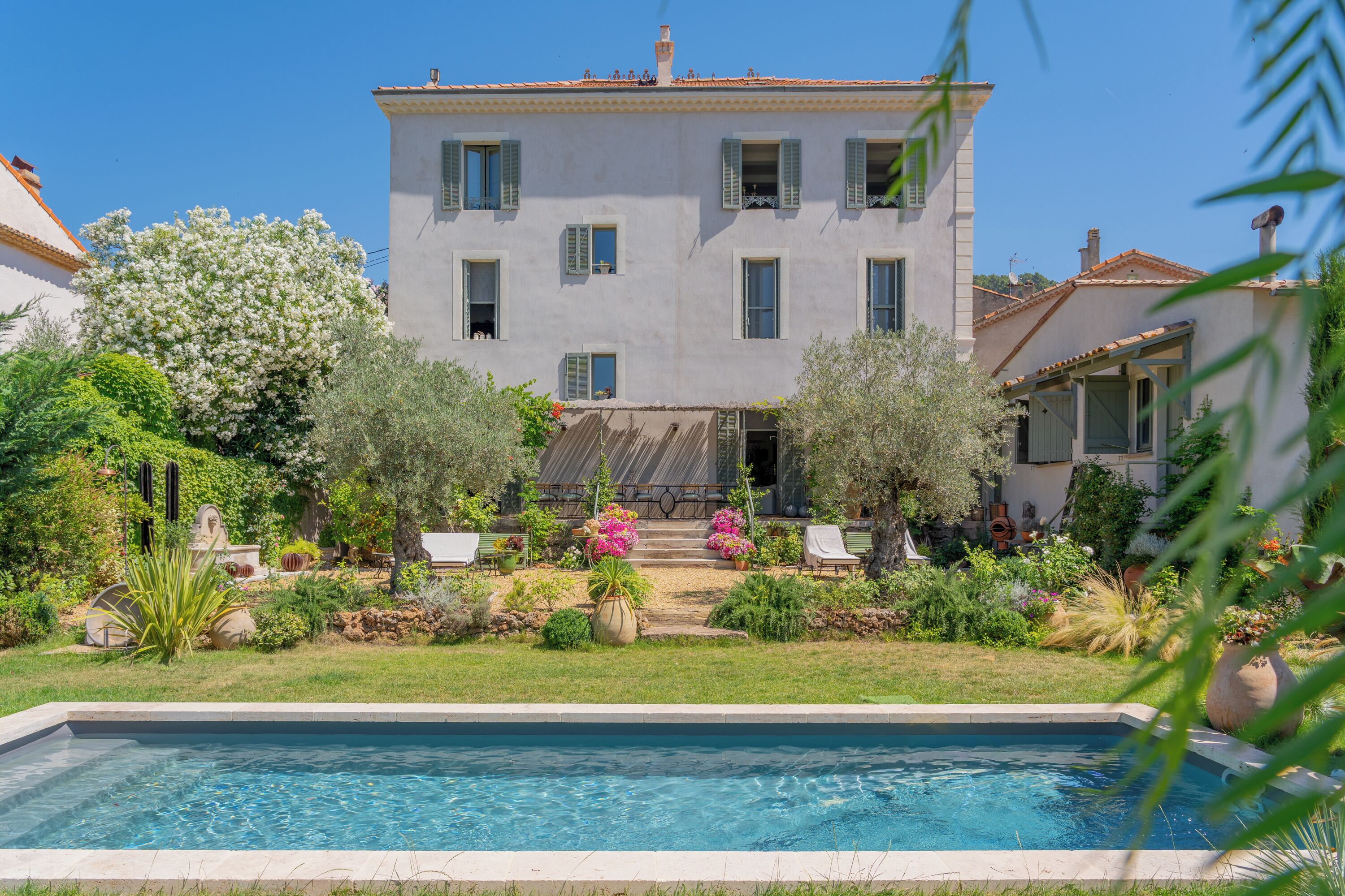 A two-story building with a swimming pool, surrounded by greenery and a well-maintained garden.