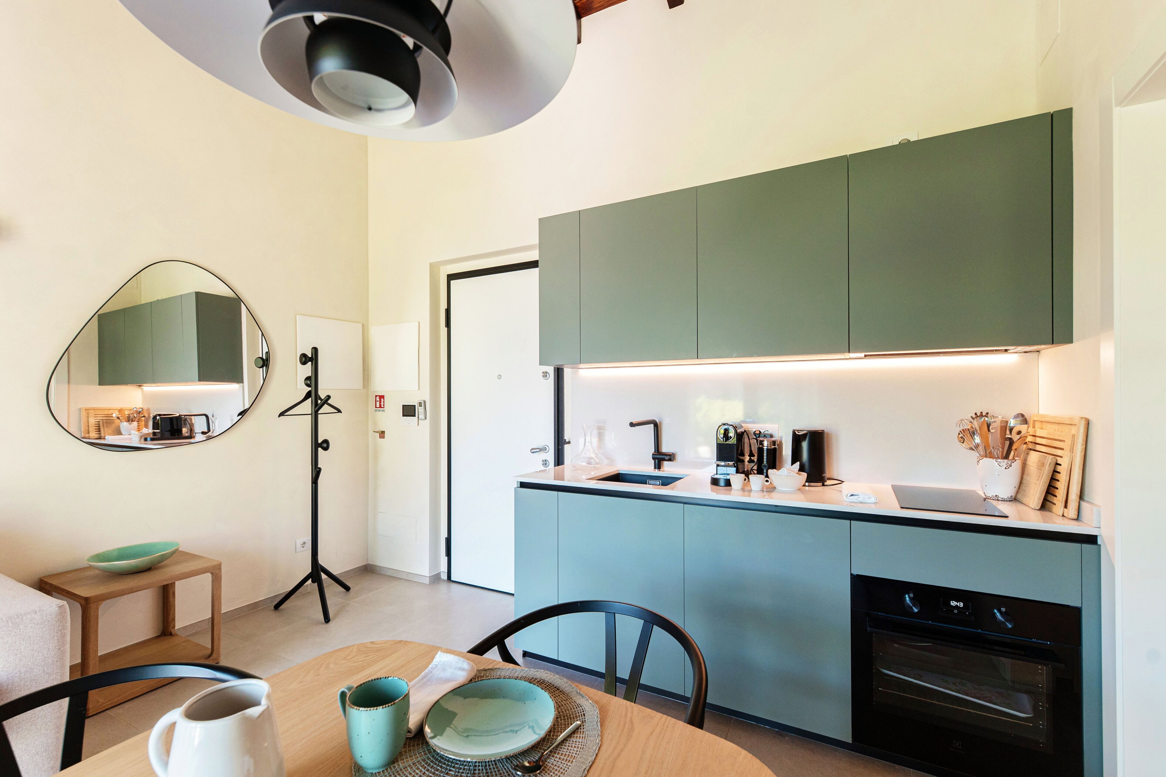 A compact kitchen with a central island, a built-in oven, and a tripod floor lamp.