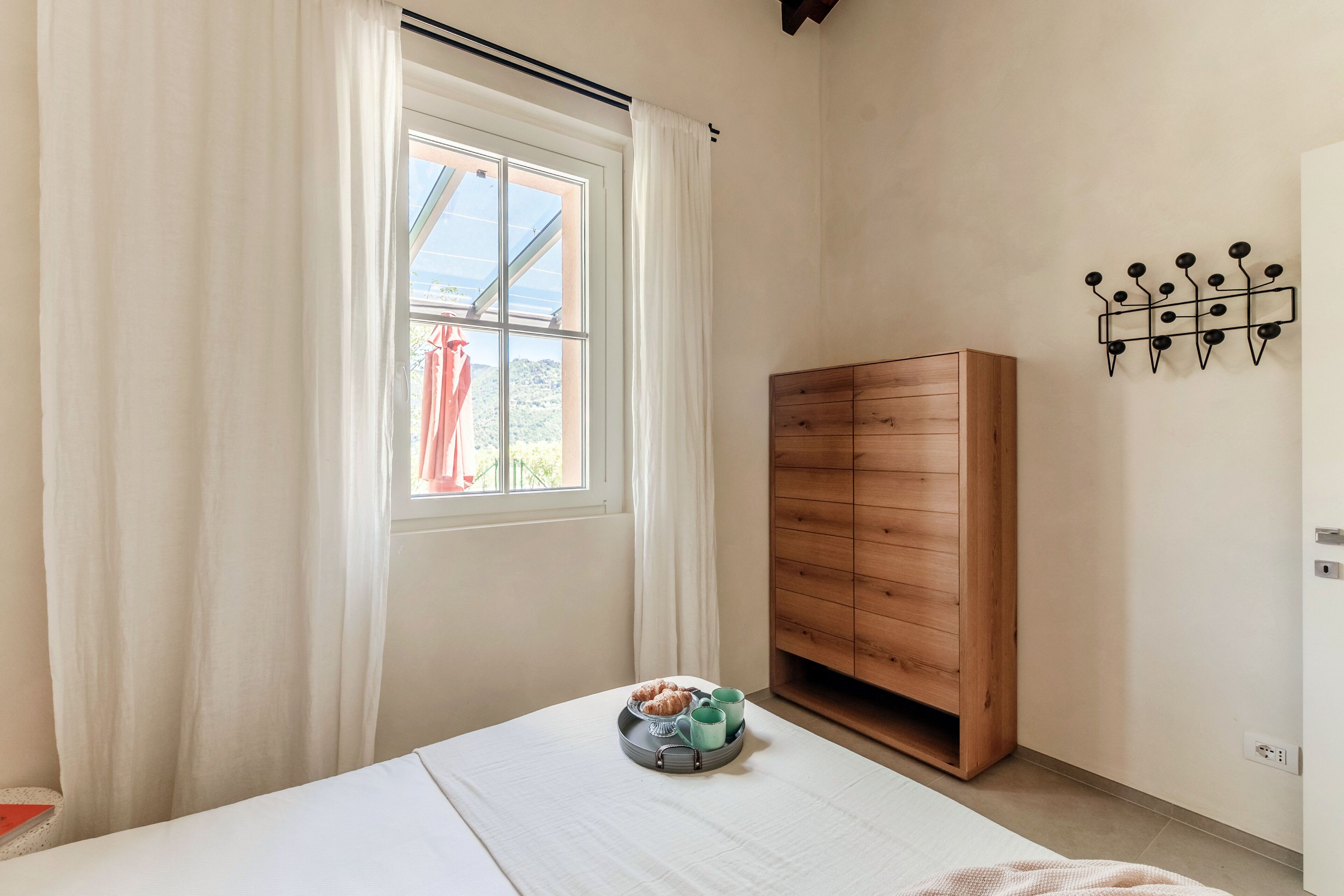 A bedroom with a bed, a wooden wardrobe, a window with curtains, and a wall-mounted hook.