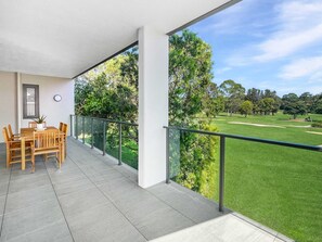 A balcony with a view of a golf course, a dining table with chairs, and a potted plant. - Scenic Batemans Bay Stay Near Golf Course (Batemans Bay)