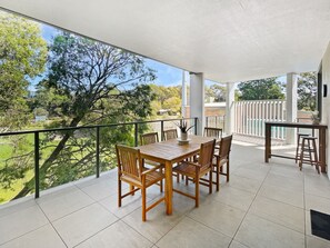 A balcony with a wooden table and chairs, a railing, and a view of greenery and buildings. - Scenic Batemans Bay Stay Near Golf Course (Batemans Bay)