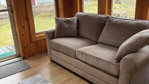 Puiset sisustuselementit, beige sohva, kuviollinen matto ja näkymä ulos.