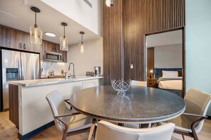 A modern kitchen with a central island, a dining area with a round table, and a bedroom with a bed and nightstand. - Capitol Peak Lodge 3518 (Snowmass Village)