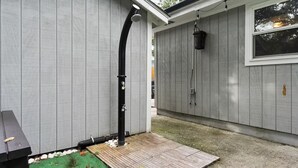 A covered outdoor area with a wooden deck, a black hose, and a hanging light fixture. - Oak Island Sun: 3 blocks to beach, fenced yard, fire pit (Oak Island)