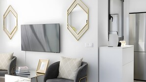 Una sala moderna con un televisor de pantalla plana, una mesa de centro, un sofá, una mesita auxiliar y una zona de cocina con un refrigerador.