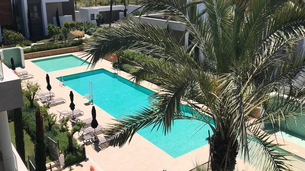 Un área de piscina con varias piscinas, tumbonas y palmeras.