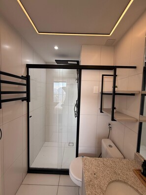 Un baño moderno con cabina de ducha de vidrio, inodoro y estantes empotrados.
