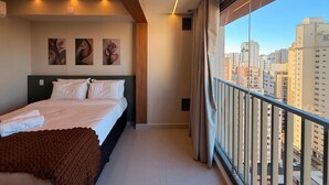 Ein modernes Schlafzimmer mit Bett, Kunstwerken und Blick auf die Stadt.