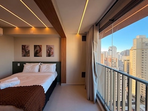 A modern bedroom with a bed, artwork, and a city view. - Studios Luxuosos Brooklin (São Paulo)