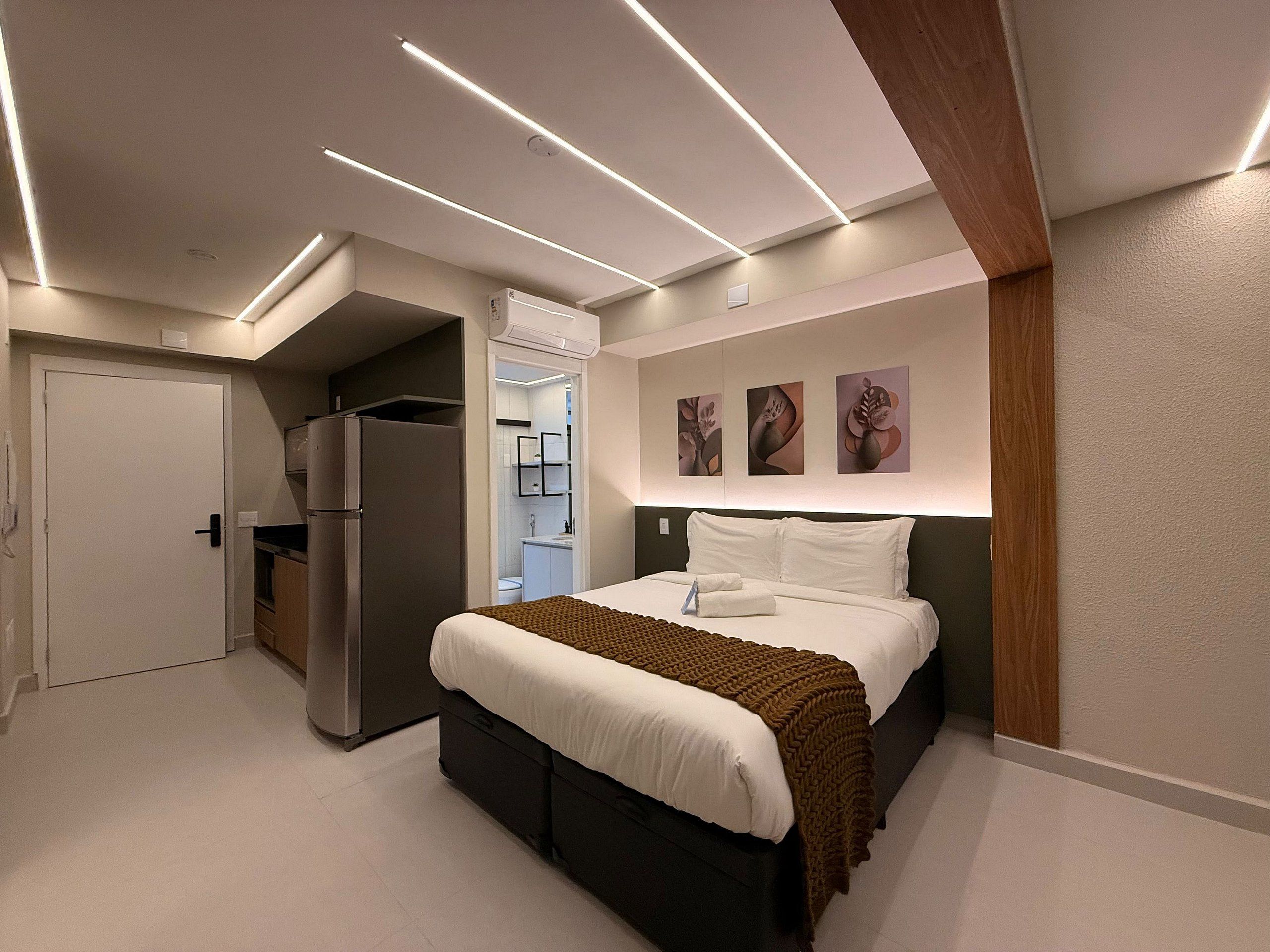 Una habitación de hotel moderna con cama, refrigerador, kitchenette y obras de arte en la pared.