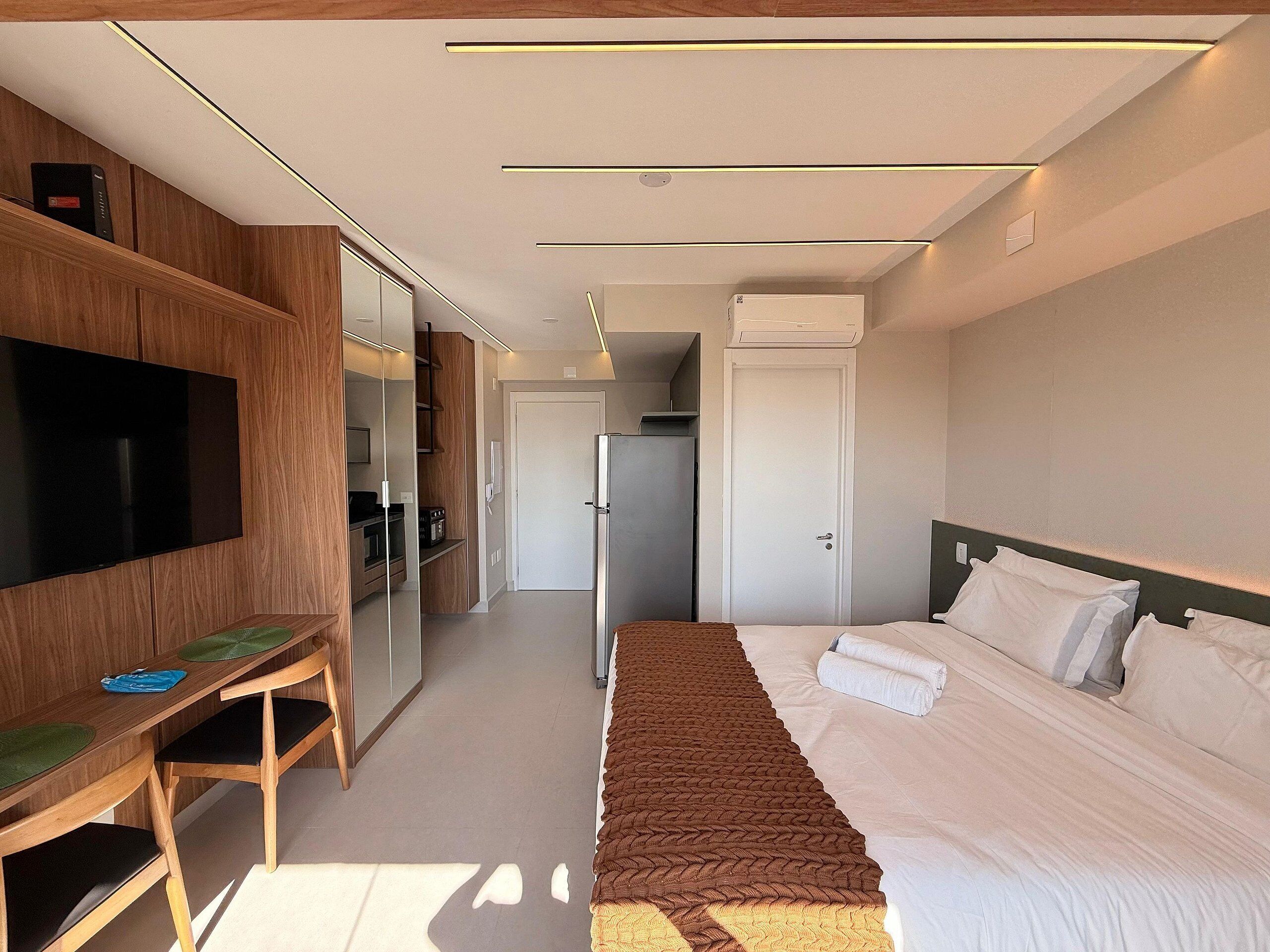 A modern hotel room with a bed, a desk, a television, and a wardrobe.
