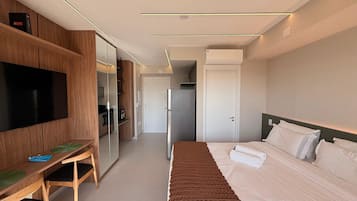 A modern hotel room with a bed, a desk, a television, and a wardrobe.