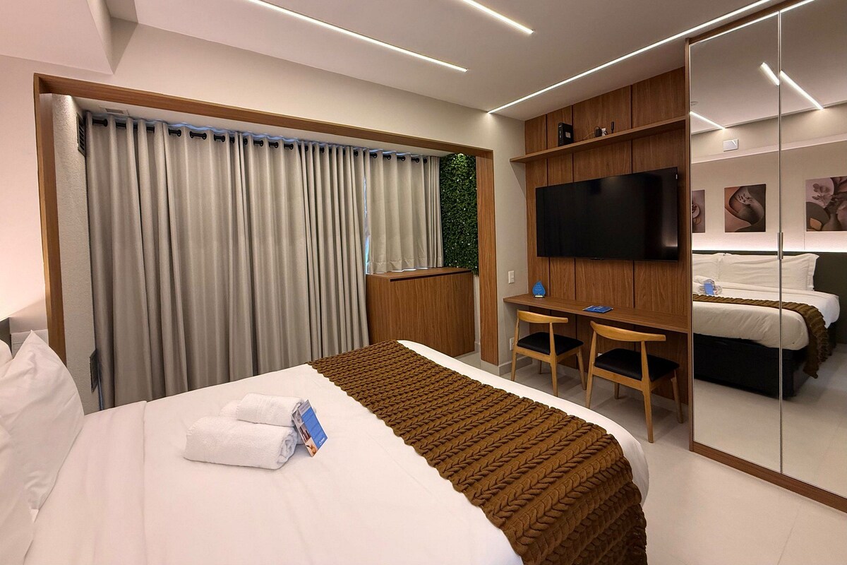 Habitación de hotel con cama, escritorio, televisor y espejo.