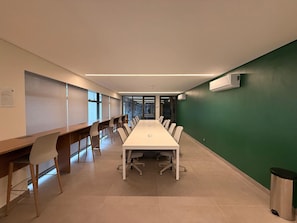 Un salón de conferencias con una larga mesa, sillas y un bote de basura.
