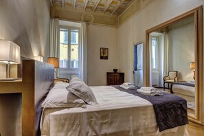 A hotel room with two beds, a large mirror, a window with curtains, and a small table with a lamp. - Fossi Apartment by Mamo Florence (Firenze)