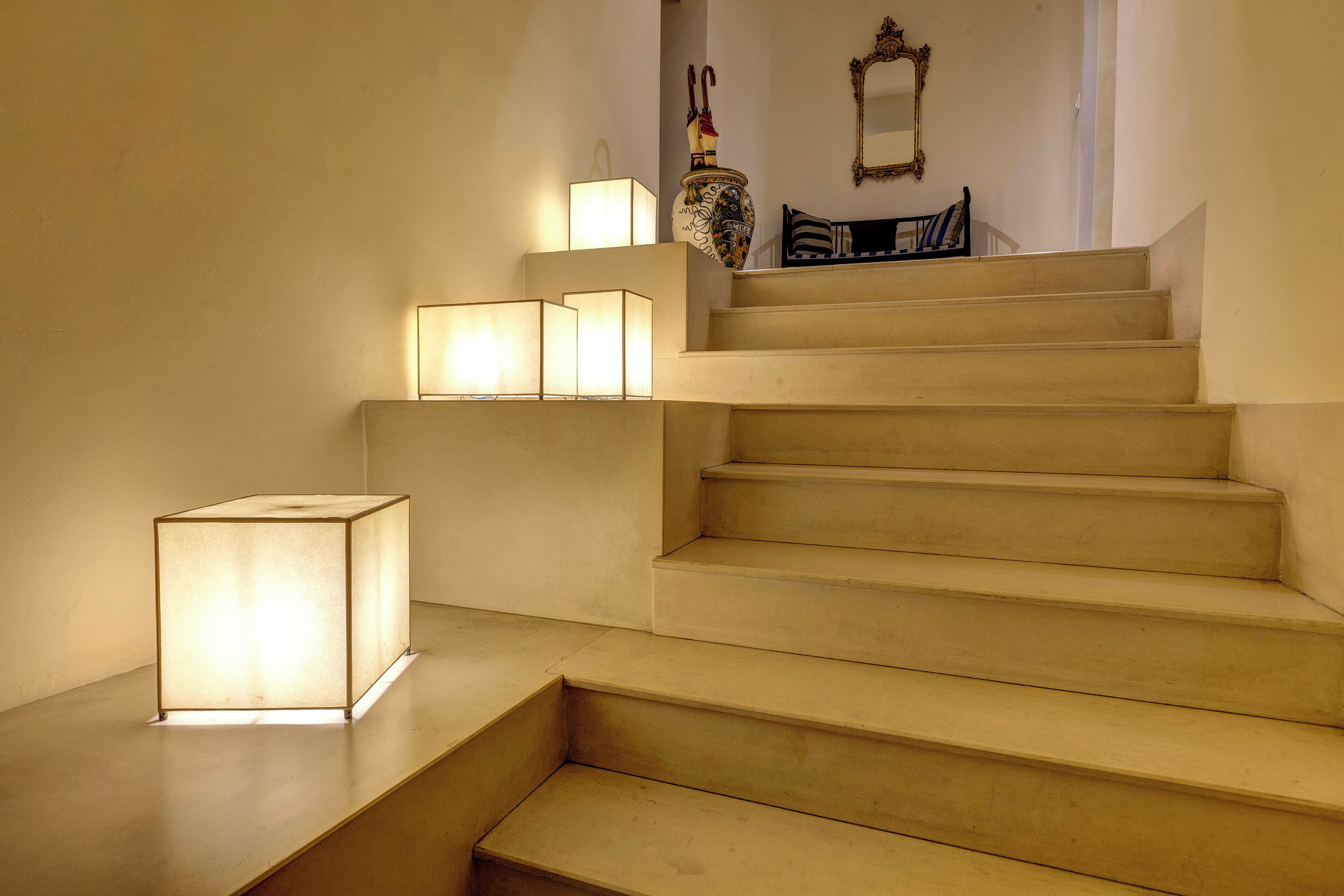 A staircase with a light fixture on the left and a chair at the top.